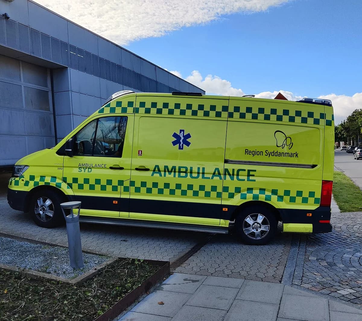 A yellow-green ambulance parked beside a building in Denmark.