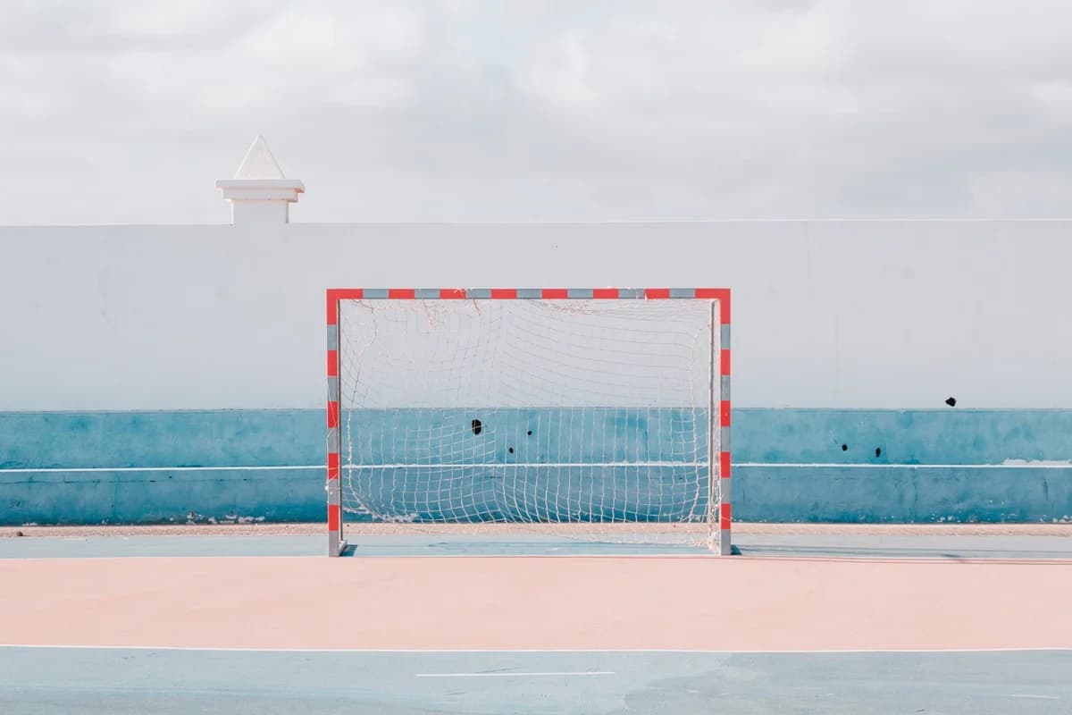 An empty outdoor handball court with a red-and-white goalpost in front of a white and blue wall.